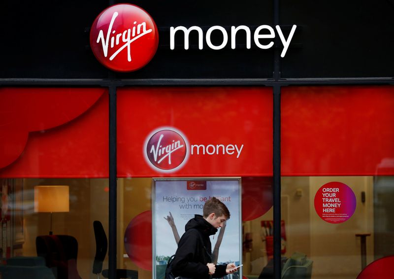 © Reuters. A man checks his phone as he walks past a branch of Virgin Money in Manchester