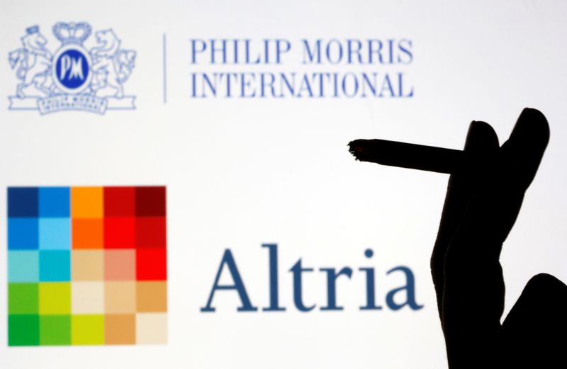© Reuters. A hand with a cigarette is seen in front of displayed logos of Philip Morris and Altria in this picture illustration