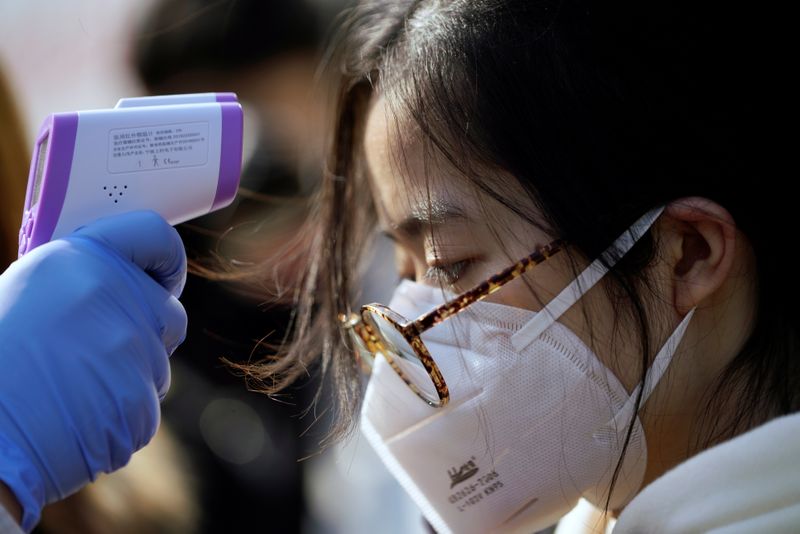 © Reuters. A worker checks the temperature of a woman at a mask factory in Shanghai