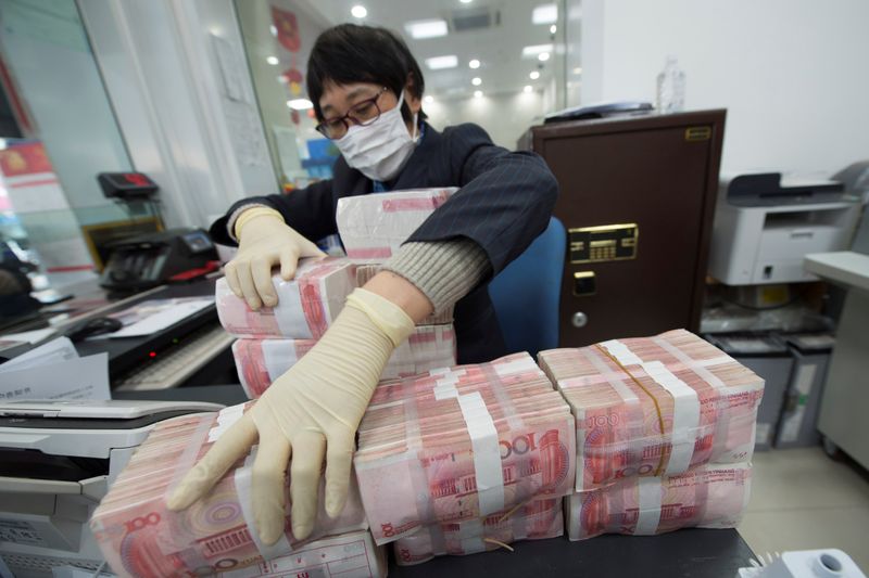 © Reuters. Staff member wearing a face mask arranges stacks of Chinese yuan banknotes at a bank in Nantong
