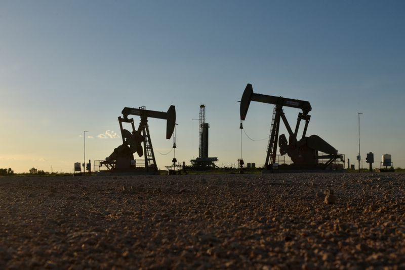 © Reuters. FILE PHOTO: Pump jacks operate in front of a drilling rig in an oil field in Midland