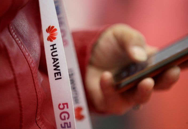 © Reuters. FILE PHOTO: An attendee wears a badge strip with the logo of Huawei and a sign for 5G at the World 5G Exhibition in Beijing