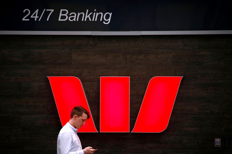 © Reuters. FILE PHOTO: A pedestrian looks at his phone as he walks past a logo for Australia's Westpac Banking Corp located outside a branch in central Sydney