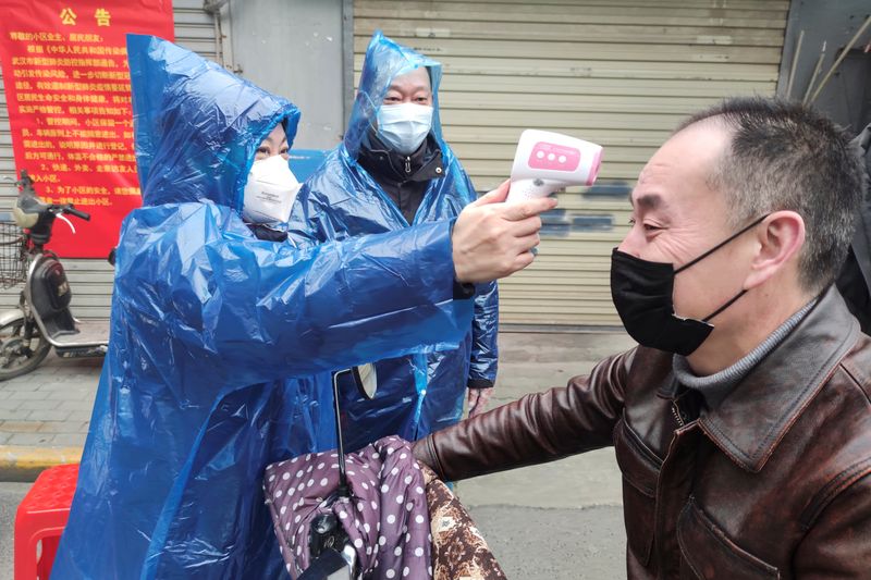 © Reuters. Funcionária mede temperatura de homem na entrada de complexo residencial em Wuhan
