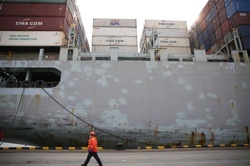 © Reuters. Worker wearing a face mask walks past a cargo ship at a container terminal of Qingdao port