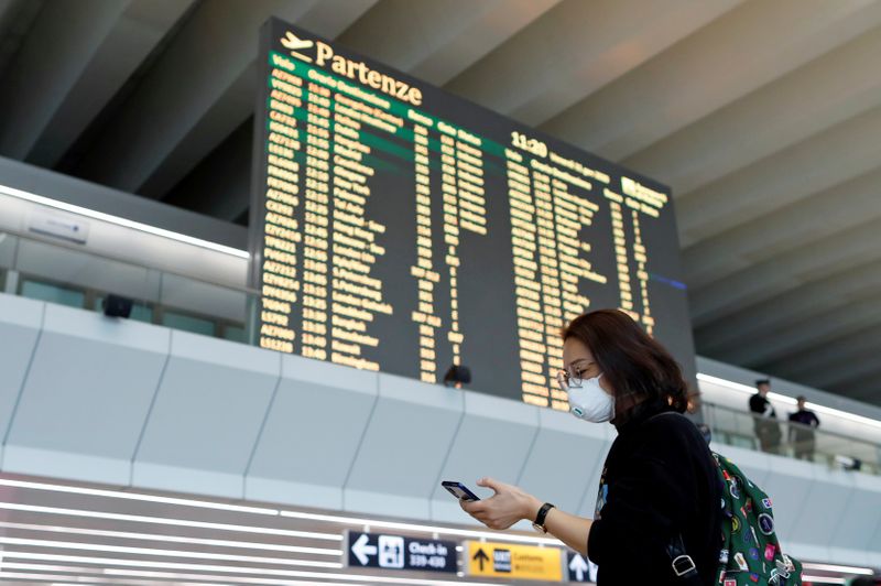 © Reuters. Passenger in a protective mask uses her phone on at Rome's Fiumicino airport