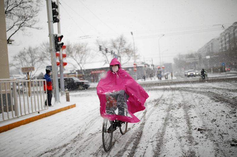 © Reuters. FILE PHOTO: Woman wearing a face mask rides a bicycle amid snow, as the country is hit by an outbreak of coronavirus, in Beijing