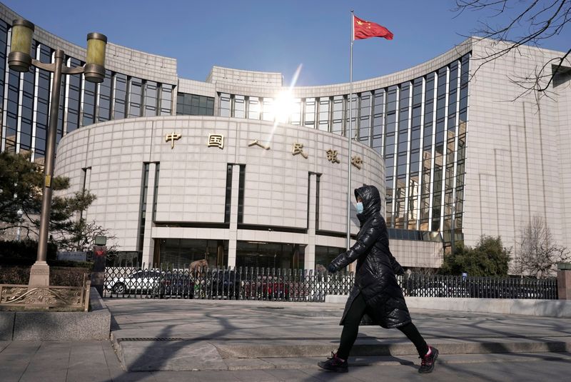 © Reuters. FOTO DE ARCHIVO: Una mujer con una máscara ante la sede del Banco Popular de China, en Pekín