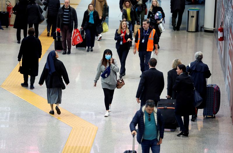 © Reuters. Una donna con una maschera protettiva cammina in mezzo alla folla all'Aeroporto di Roma Fiumicino