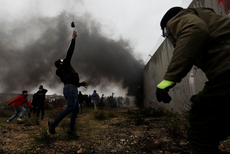 © Reuters. A Palestinian demonstrator hurls stones at Israeli forces as he stands next to the Israeli barrier during a protest against Trump's Middle East peace plan, in the village of Bilin in the Israeli-occupied West Bank