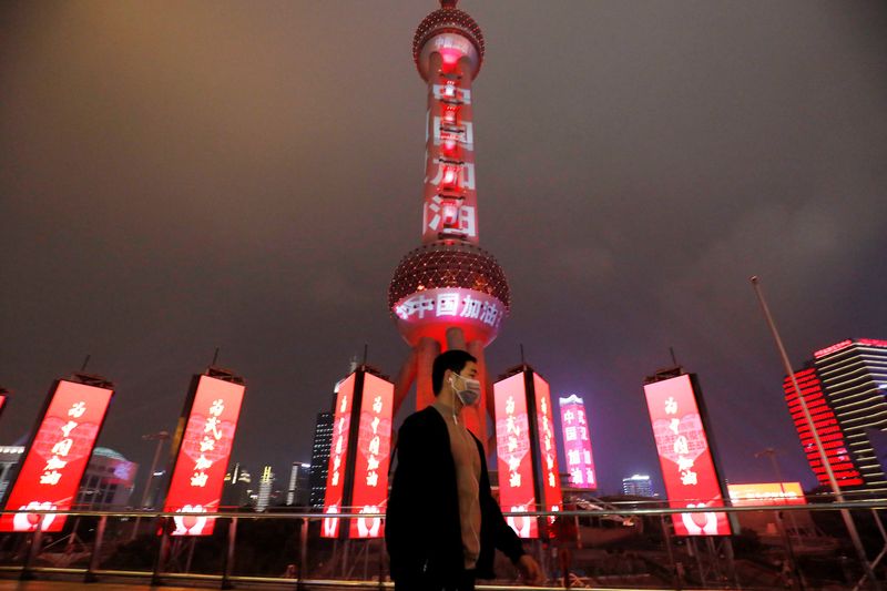 © Reuters. Man wearing a face mask walks past the Oriental Pearl Tower lit with messages reading "Stay strong China", on the Lantern Festival in Shanghai