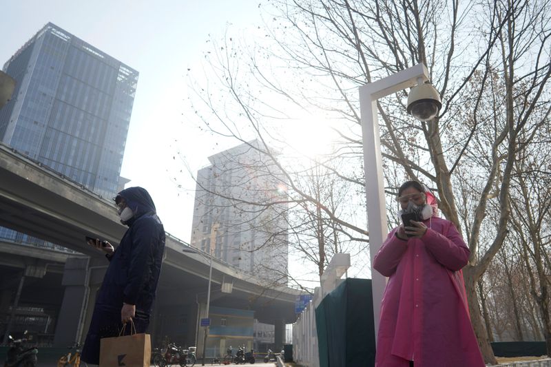 © Reuters. Pedestrians wearing masks stand under a surveillance camera as they wait to cross a road after the extended Lunar New Year holiday caused by the novel coronavirus outbreak, in Beijing's central business district