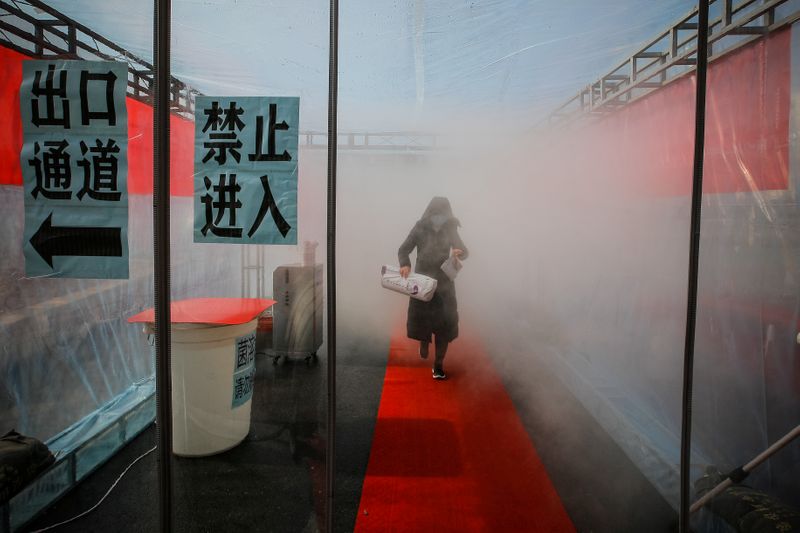 © Reuters. Woman wearing a face mask walks through a device that sprays disinfectant at an entrance to a residential compound in Tianjin