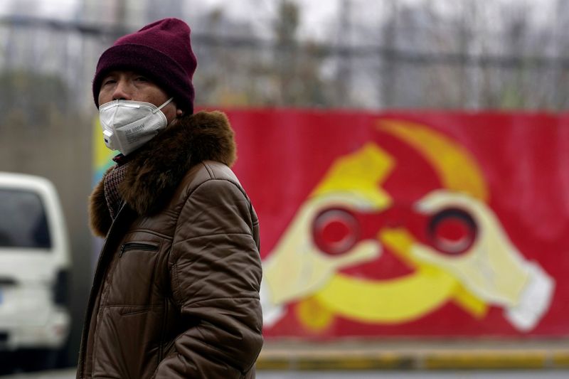 © Reuters. FILE PHOTO: A man wears a mask as he walks past a mural showing a modified image of the Chinese Communist Party emblem in Shanghai