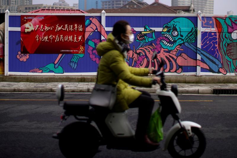© Reuters. FILE PHOTO: A woman wearing a mask is seen in front of a wall painted with graffiti at a construction site in Shanghai
