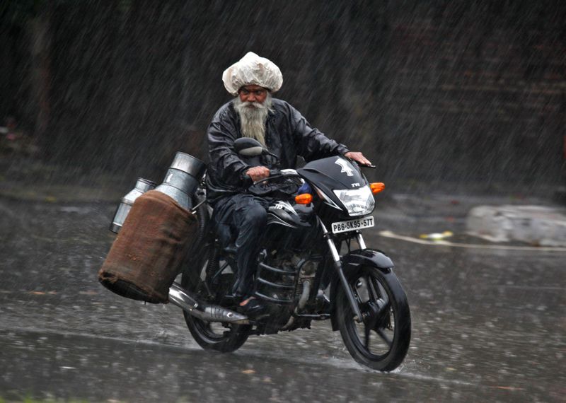 © Reuters. FILE PHOTO: A milkman rides a motorcycle during a heavy rain shower in Chandigarh