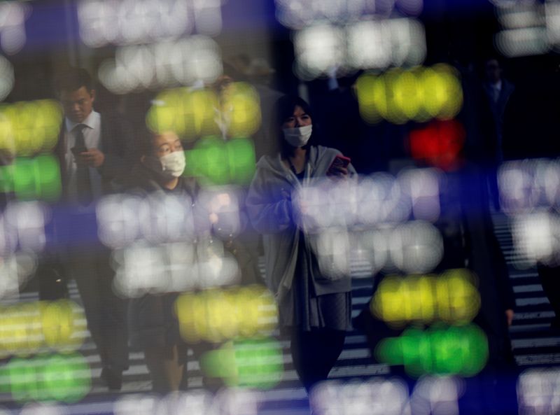 © Reuters. Pedestrians wearing facial masks are reflected on an electric board showing stock prices outside a brokerage at a business district in Tokyo