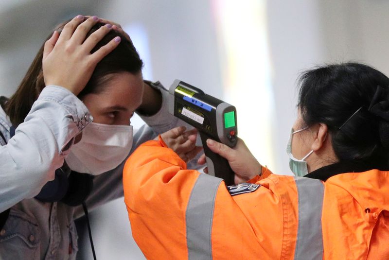 © Reuters. FILE PHOTO: A worker checks the temperature of a passenger arriving into Hong Kong International Airport with an infrared thermometer