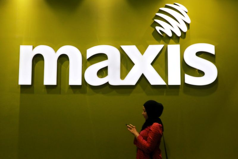 © Reuters. FILE PHOTO: A woman walks past a logo of Maxis at its headquarters in Kuala Lumpur