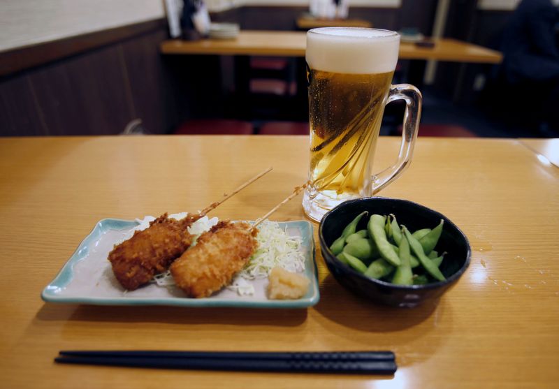 © Reuters. Typical combination of beer, deep fried meat on skewers and green soybeans are seen on a table at "Ikken me sakaba", a discount izakaya bar offering cheap food and drinks, in Tokyo