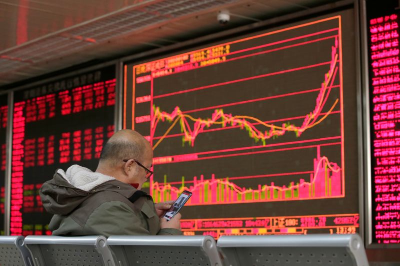 © Reuters. An investor looks at his mobile phone in front of a board showing stock information at a brokerage office in Beijing