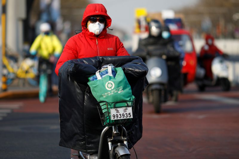 © Reuters. A woman wearing a face mask rides a scooter along a street, as the country is hit by an outbreak of the new coronavirus, in Beijing