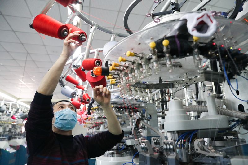 © Reuters. El empleado que usa una máscara facial trabaja en una línea de producción que fabrica calcetines para exportar en una fábrica en Huzhou