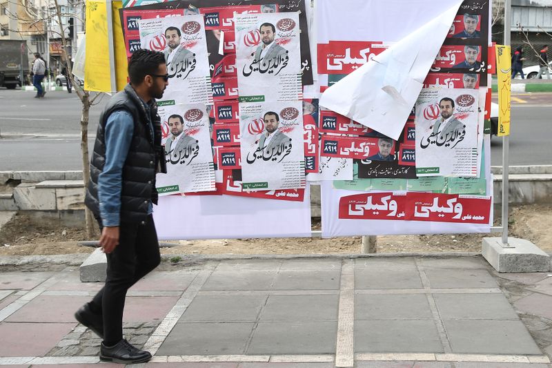 © Reuters. A man walks past parliamentary election campaign posters in Tehran