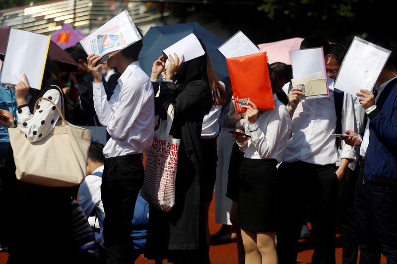 © Reuters. FILE PHOTO: Students shield themselves from the sun as they line up at a job fair at a university in Guangzhou