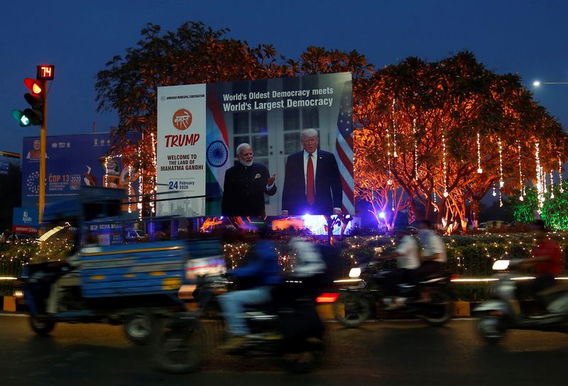 © Reuters. People ride their motorbikes past a hoarding with the images of India's Prime Minister Narendra Modi and U.S. President Donald Trump, in Ahmedabad