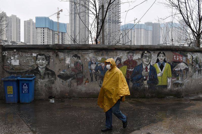 © Reuters. FOTO DE ARCHIVO: Un hombre con mascarilla pasa por delante de un mural cerca de una obra en construcción en Wuhan en la provincia de Hubei, China, el 28 de febrero de 2020