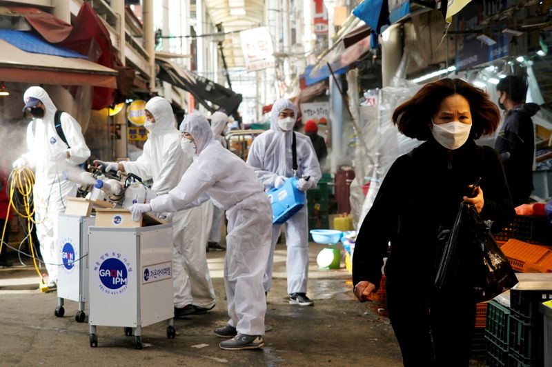 © Reuters. FILE PHOTO: A woman wearing a mask to prevent contracting the coronavirus reacts as employees from a disinfection service company sanitize a traditional market in Seoul