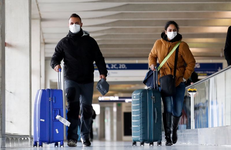 © Reuters. FILE PHOTO: People wearing protective face masks walk as they arrive at Charles de Gaulle airport near Paris