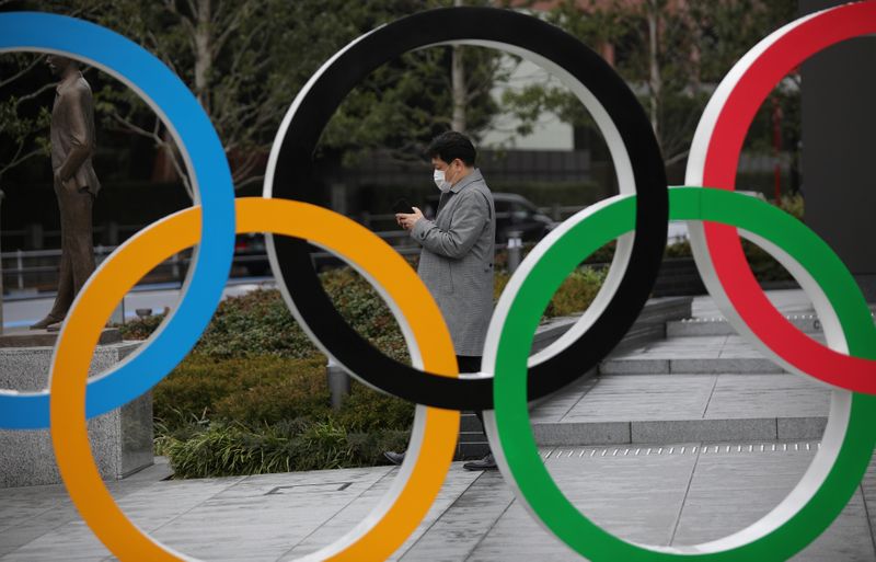 © Reuters. Un hombre con mascarilla mira su móvil junto a una escultura de los aros olímpicos en Tokio