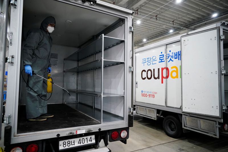 © Reuters. A worker in a protective gear sanitizes a vehicle before leaving to deliver packages in Incheon