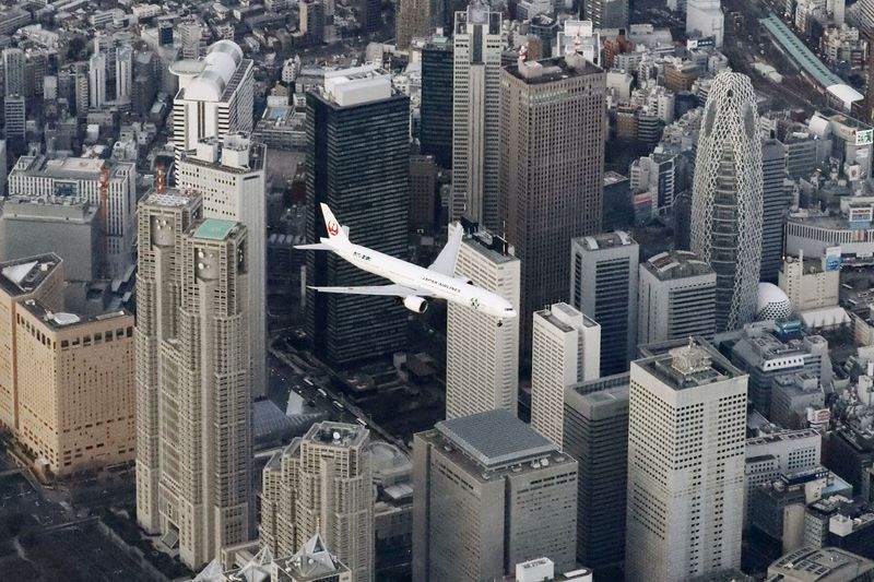 © Reuters. An aerial view shows an airplane flying over skyscrapers in a test of the new flight paths for international passenger aircraft bound for Haneda Airport, at Shinjuku district in Tokyo, Japan