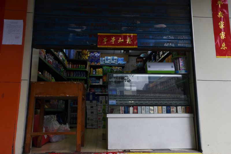 © Reuters. Man wearing a face mask stands inside a shop with the roller shutter half closed, in Wuhan, the epicentre of the novel coronavirus outbreak