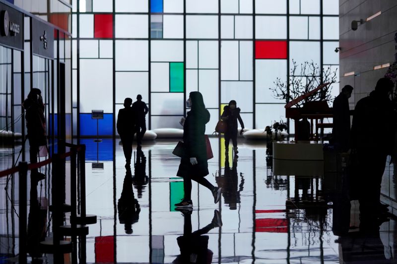 © Reuters. FILE PHOTO: People wearing face masks walk inside an office building at the Lujiazui financial district in Pudong