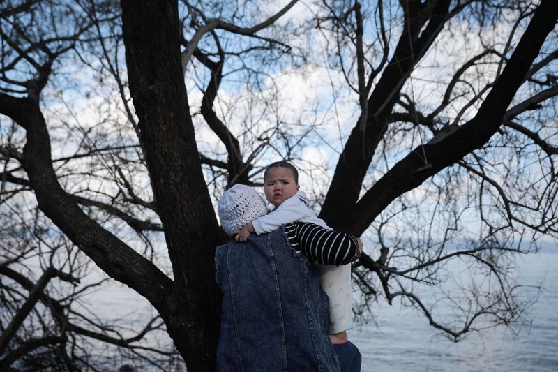 © Reuters. A woman holds a baby, as migrants who arrived the previous day on a dinghy after crossing part of the Aegean Sea from Turkey, are sheltered near the village of Skala Sikamias, on the island of Lesbos