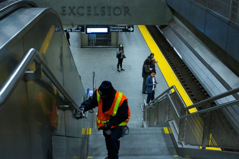 © Reuters. A woman wearing a face mask waits for the train as a MTA worker disinfects a subway station in the Manhattan borough of New York City, New York