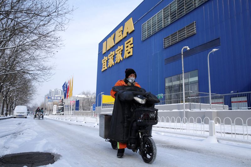 © Reuters. Clean worker wearing a face mask drives past a closed IKEA store in Beijing