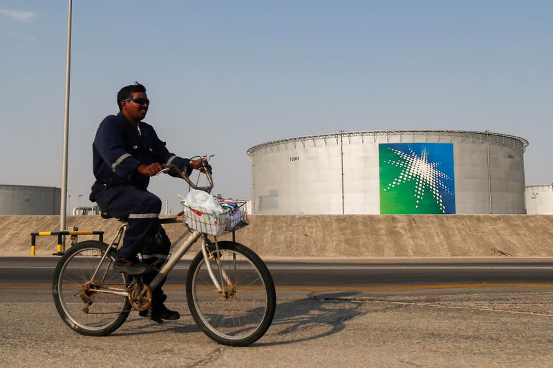 © Reuters. An employee rides a bicycle next to oil tanks at Saudi Aramco oil facility in Abqaiq