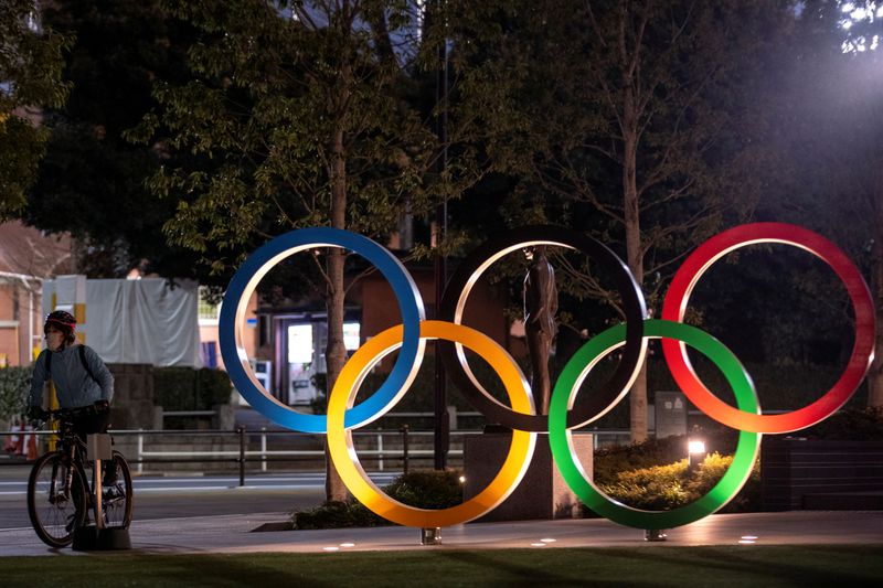 © Reuters. A woman wearing a protective face mask, following the outbreak of the coronavirus, rides her bicycle past The Olympic rings in front of the Japan Olympics Museum in Tokyo