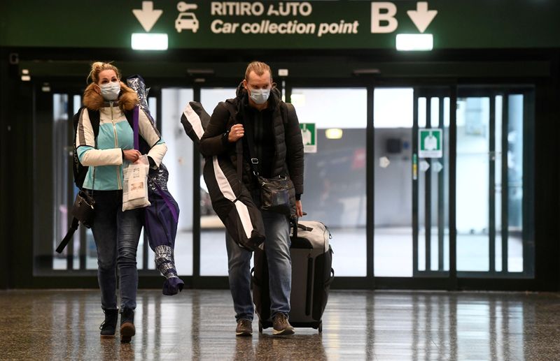 © Reuters. People wearing protective masks walk in Malpensa airport near Milan