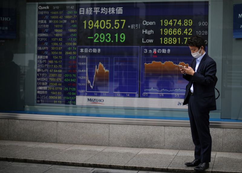 © Reuters. A man wearing protective face mask stands in front of a stock quotation board outside a brokerage in Tokyo