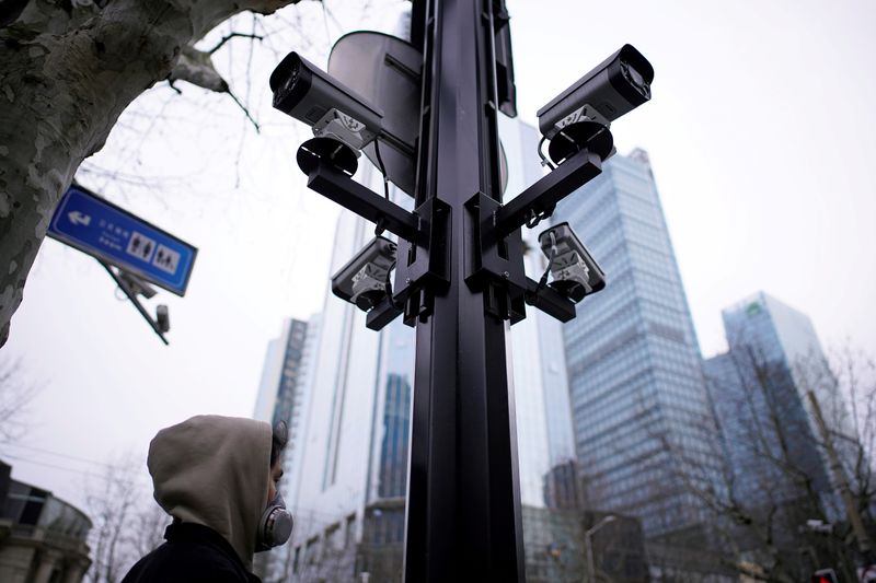 © Reuters. FILE PHOTO: A man wearing a protective face mask walks under surveillance cameras as the country is hit by an outbreak of the novel coronavirus, in Shanghai