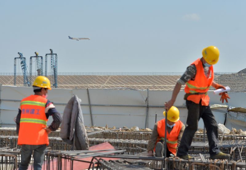 © Reuters. Workers wearing face masks are seen at a construction site for the expansion of Guiyang Longdongbao International Airport as an airplane flies over, in Guiyang, Guizhou