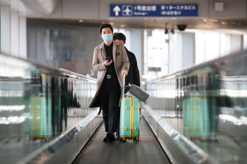 © Reuters. Passengers wearing face masks stand on a moving walkway at Beijing Capital International Airport as the country is hit by an outbreak of the novel coronavirus