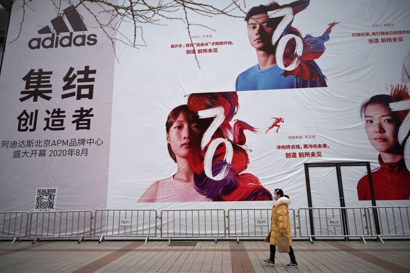 © Reuters. Mulher com máscara de proteção contra coronavírus passa por banner da Adidas em Pequim, China