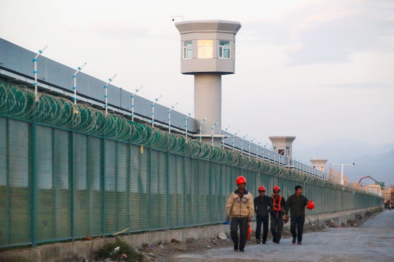 © Reuters. Workers walk by the perimeter fence of what is officially known as a vocational skills education centre in Dabancheng